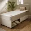 Candy-1-150x150 - Jamies Furniture White platform bed with built-in under-bed storage drawers in a bright bedroom, with a potted plant and beige cushions nearby.