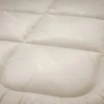 Close-up of a white quilted fabric with padded rectangular sections, like a comforter or duvet cover.