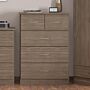 100-102-119 1 - Jamies Furniture Tall wooden dresser with five drawers in a medium brown finish, placed in a bedroom corner with a small clock on top.