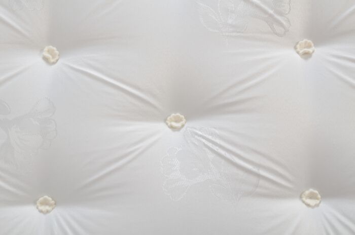 White quilted fabric with tufted buttons and subtle floral embroidery patterns.