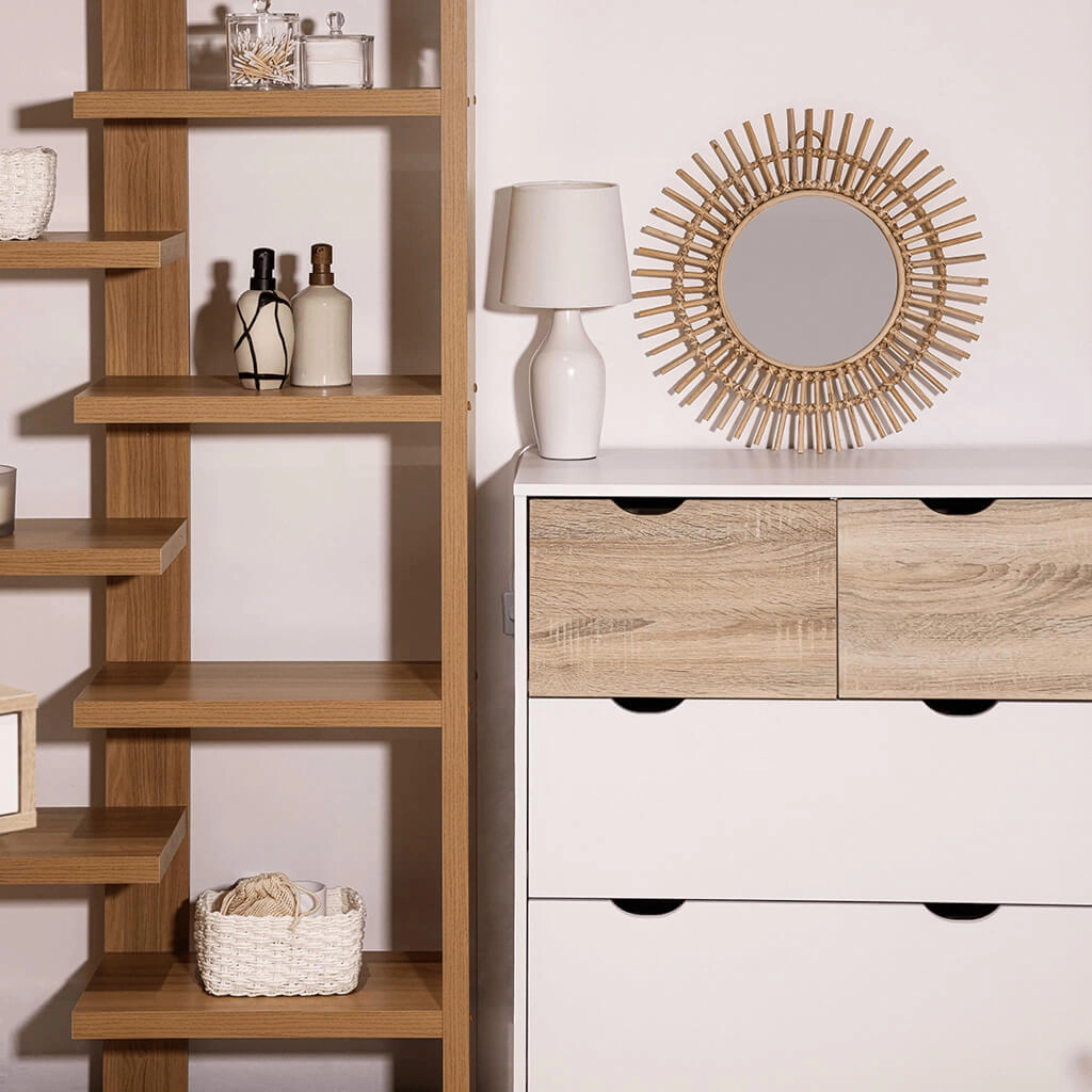 Wooden open shelving unit beside a white dresser, topped with a white lamp and a round sunburst mirror. A small basket sits on a lower shelf.